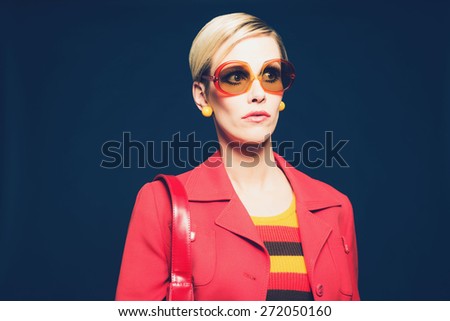 Close up Stylish Blond Woman in Red Blazer with Sunglasses and Shoulder Bag, Looking to the Right Seriously on a Dark Blue Background.