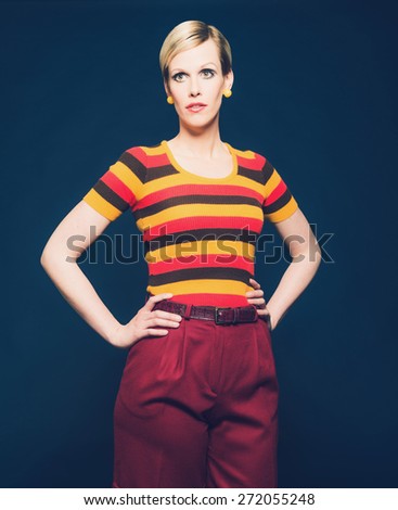 Portrait of a Pretty Blond Woman Posing in Casual Striped Shirt and Short Pants with Hands on Waist, Isolated on Dark Blue Background.