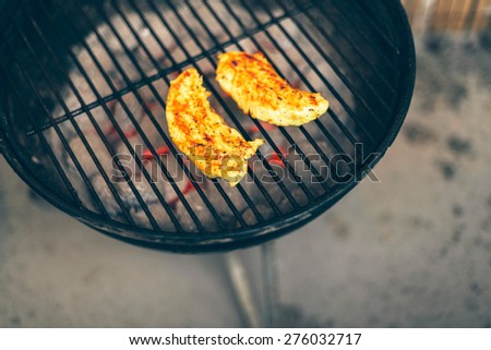 Two healthy lean seasoned chicken breasts grilling on a BBQ outdoors in a backyard, high angle view