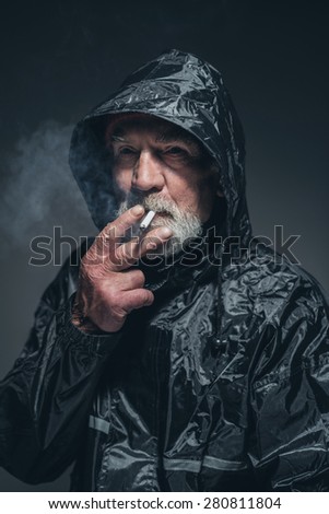 Close up Thoughtful Bearded Senior Man Wearing Black Waterproof Jacket with Smoke Looking Afar While Thinking of Something. Captured in Studio with Black Background.