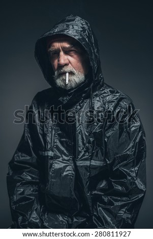 Portrait of a Reflective Senior Man in Black Rain Jacket, Smoking a Cigarette While Looking Into Distance.