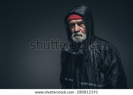Bearded Adult Man Wearing Black Waterproof Jacket, Looking at the Camera Seriously Against Black Background with Copy Space.