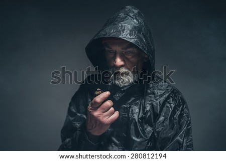 Close up Pensive Adult Man in Rain Jacket with Cigarette Pipe, Looking Down While Thinking So Deep Against Black Background.