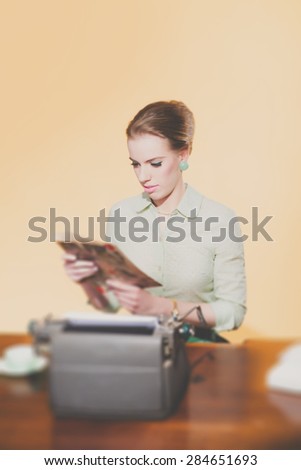 Retro 1950 young secretary woman sitting behind desk reading magazine.