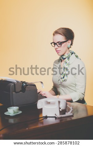 Vintage 1950 young secretary woman behind desk typing on typewriter wearing black glasses.