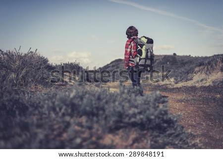 Backpacker wearing a large backpack of camping gear walking through hilly scrub standing facing away from the camera surveying his surroundings