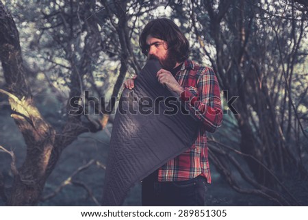 Backpacker setting up camp for the night unrolling his sleeping mat in a wooded area with trees