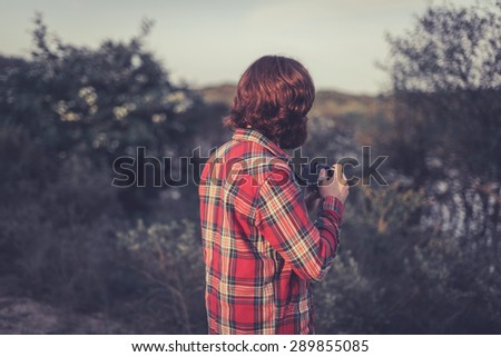 Wildlife photographer out in the wilderness standing with his back to the camera watching an area of trees and scrub