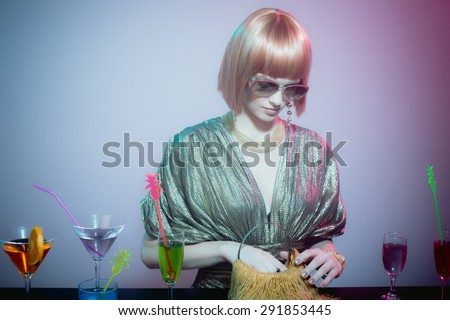 Glamorous Woman Wearing Sunglasses and Shiny Retro Gown Looking Through Purse at Cocktail Covered Bar in Smoky Disco Night Club