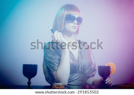 Glamorous and Sophisticated Woman with Red Hair Wearing Sunglasses and Shiny Retro Gown Standing at Bar Smoking Cigarette and Gambling in Smoky Disco Night Club