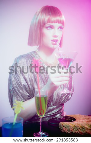 Glamorous Woman with Short Red Hair Wearing Shiny Retro Gown and Sipping Purple Cocktail Drink from Straw in Smoky Disco Night Club