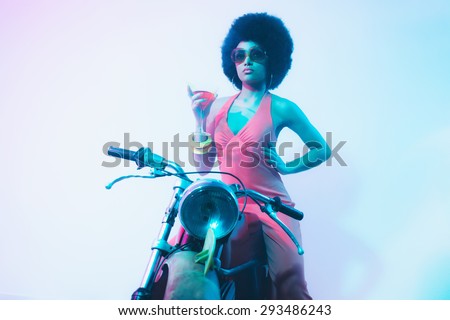 Elegant Lady with Curly Short Hair, Holding a Cocktail on her Vintage Motorcycle While Looking Into Distance Against White Background.
