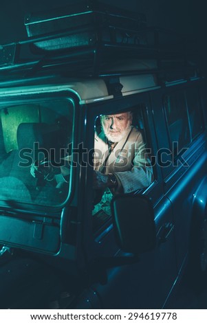 Serious Bearded Senior Man Looking at the Rear View Mirror While Driving his Four-Wheel Vehicle at Night.
