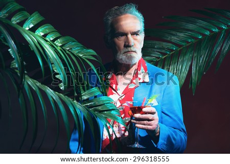Close up Serious Bearded Businessman in a Tropical Night Party, Holding a Drink Between Palm Trees and looking Into the Distance.