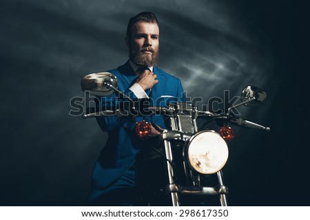 Handsome bearded businessman in a blue suit sitting waiting on a motorbike in the darkness looking thoughtfully, with copyspace