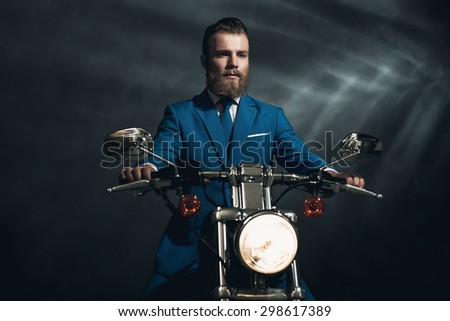 Handsome bearded businessman in a blue suit sitting waiting on a motorbike in the darkness looking thoughtfully, with copyspace