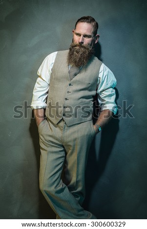 Three Quarter Shot of a Pensive Bearded Man in Formal Wear Looking Into the Distance with Hands in the Pockets Against Gray Wall.
