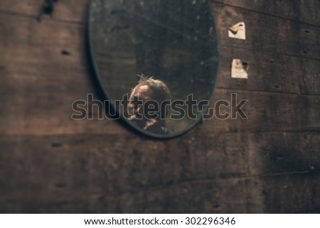 Reflection of an elderly man in a mirror hanging on a wooden wall in an old rustic barn or house, with copyspace