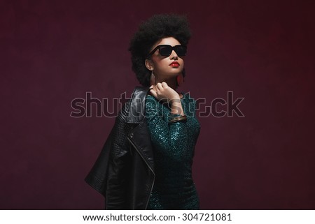 Half Body Shot of a Stylish Young Woman with Afro Hair, Holding her Jacket over the Shoulder against Maroon Background.