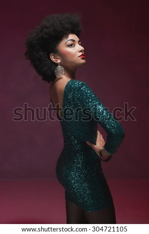 Rear View of a stylish young African American woman in an elegant green evening dress against maroon background.