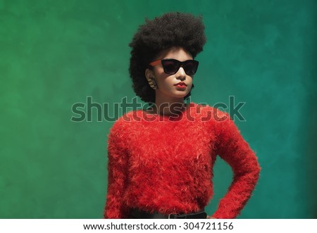 half body shot of a stylish young woman in fuzzy red tops with sunglasses, looking into the distance against green wall background.