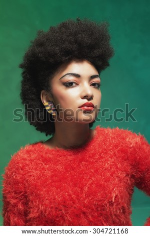 Portrait of a Young Woman with Afro Hair, Wearing Furry Red Tops, Looking at the Camera Against Green Wall Background.