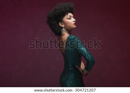 Rear View of a stylish young African American woman in an elegant green evening dress against maroon background.