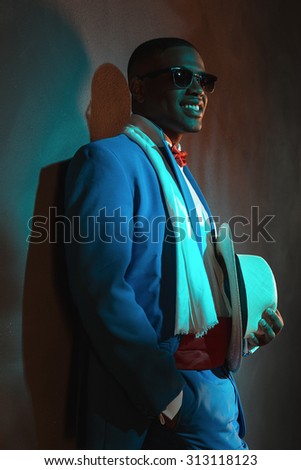 Retro african american man in blue suit wearing sunglasses. Leaning against gray wall.