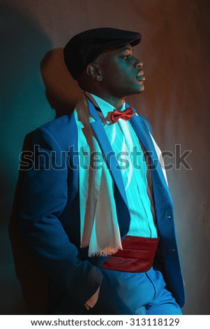 Retro african american man in blue suit wearing blue cap. Leaning against gray wall.