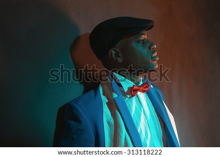 Retro african american man in blue suit wearing blue cap. Leaning against gray wall.