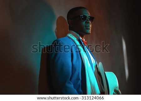 Retro african american man in blue suit wearing sunglasses. Leaning against gray wall.