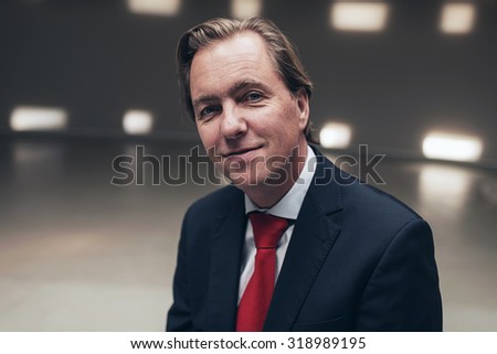 Happy young businessman wearing suit with red tie in empty room.