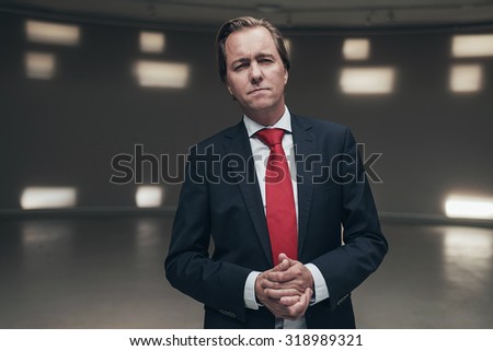 Concerned entrepreneur wearing suit with red tie standing in empty room.