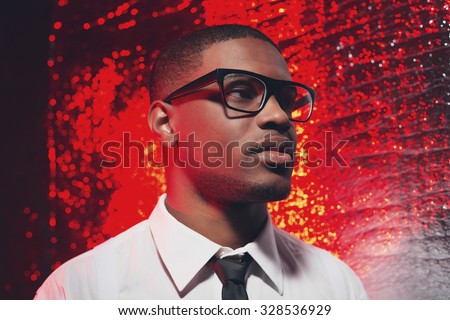 Retro fifties hispanic man with glasses in white shirt and black tie. Against red reflective background.