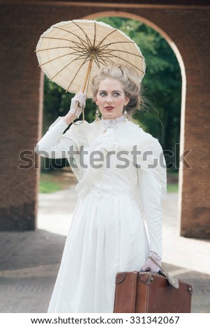 Victorian fashion girl with umbrella standing in front of gate.