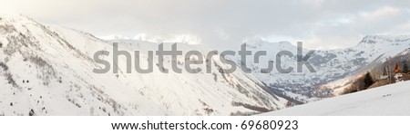 Panorama of alpine winter scenery with chalets under blue cloudy sky