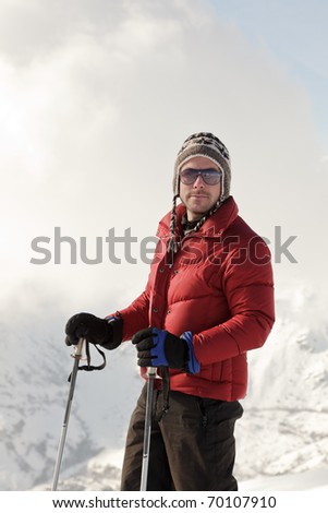 Young man with sunglasses and woolen hat standing in winter mountain landscape. Alps. France. Saint Jean d\'Arves.