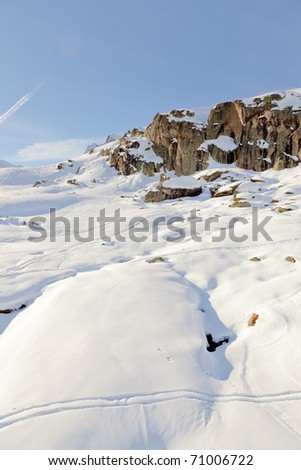 Winter mountain landscape with big rock under blue sky with sun rays. Alps. France.