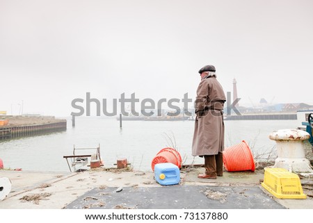 Senior man with raincoat and hat standing in dock. Lonely. Lost.