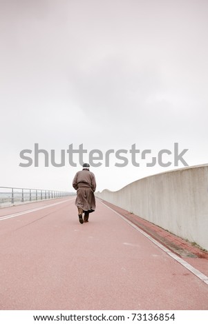 Lonely senior man with raincoat and hat walking on road. Lost.