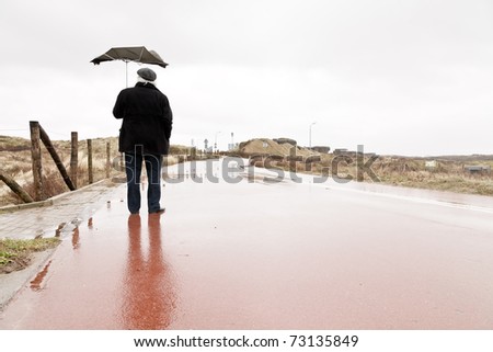 Senior man with broken umbrella by the wind standing on wet road.