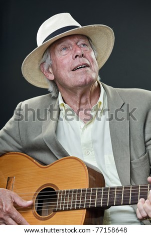 Studio portrait of senior man with hat playing acoustic guitar. Jazz musician.