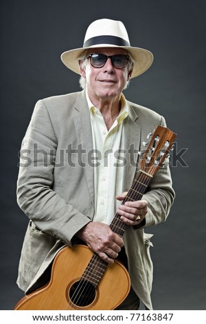 Studio portrait of senior man with hat sunglasses and guitar. Jazz musician.