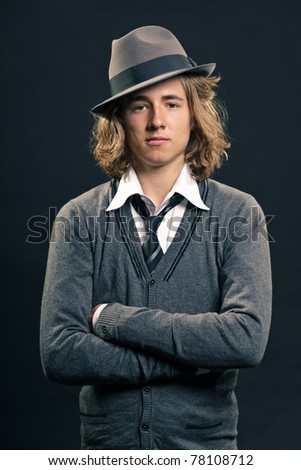 Studio portrait of cool hip looking young man with long blond hair wearing hat.