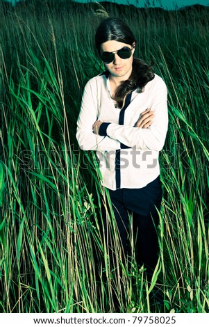 Young man with sunglasses and long brown hair standing in field with long grass. Stormy cloudy sky.
