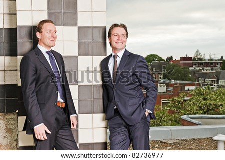 Two young business outdoors on top of building with cloudy sky.