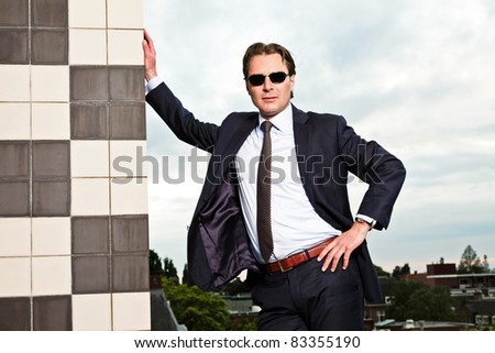 Young business man with sunglasses outdoors on top of building with cloudy sky.