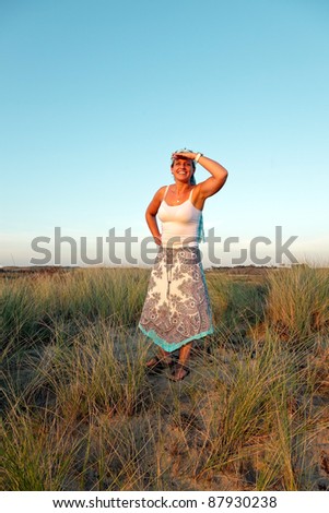 Young casual woman enjoying nature in dune landscape at sunset.