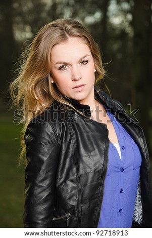 Portrait of pretty young woman with long blond hair in winter forest wearing black leather jacket and blue