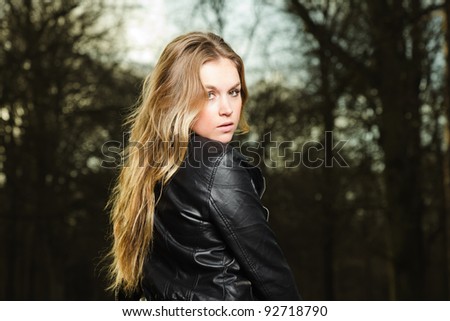 Pretty young woman long blond hair in winter forest wearing black leather jacket and blue shirt